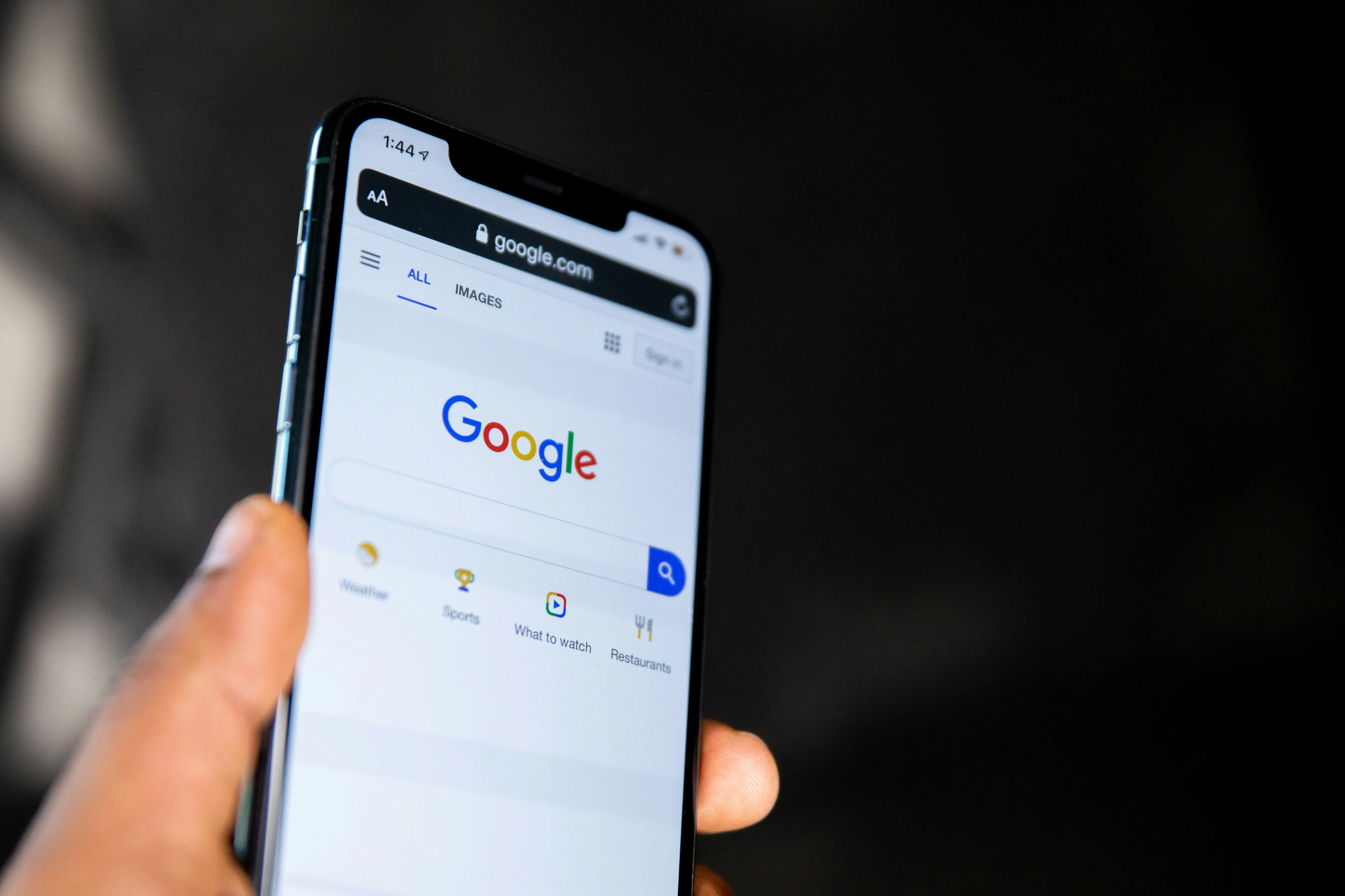 O mână care ține un smartphone afișând pagina de căutare Google, cu un cursor pe prima poziție și un grafic ascendent în fundal, simbolizând succesul în SEO.